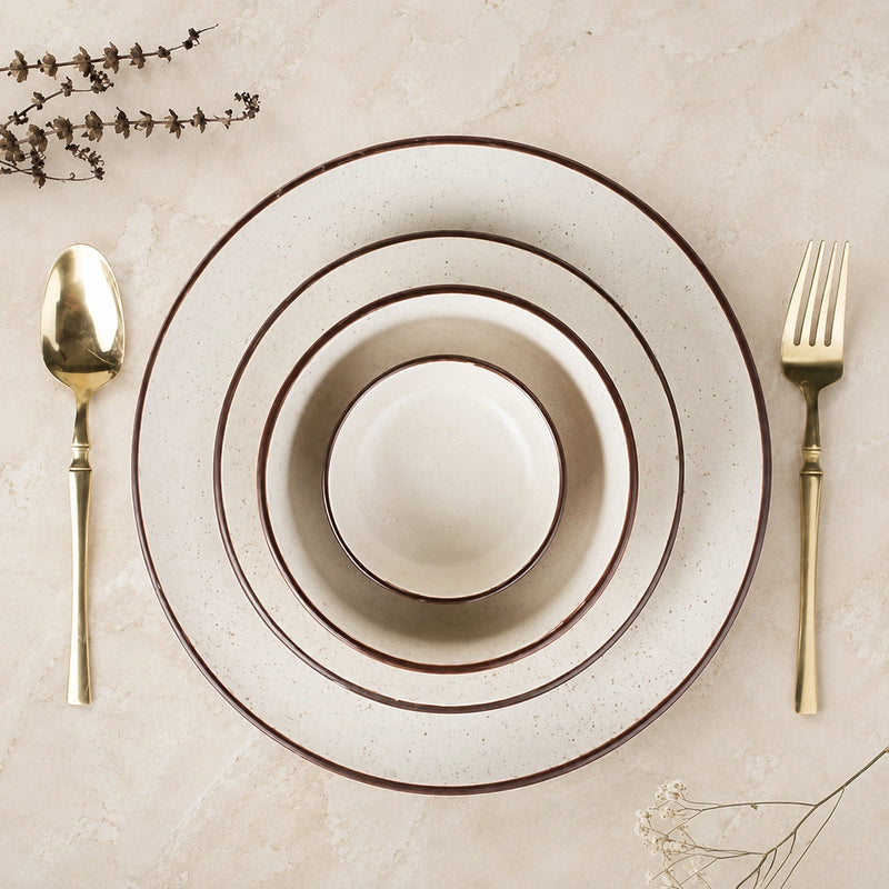 Set of ceramic plates with gold cutlery on a beige surface