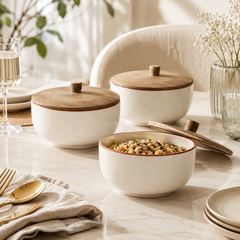 Three speckled cream ceramic bowls with light brown wooden lids are arranged on a softly lit dining table. One bowl in the foreground contains food, with its lid beside it, while two more bowls sit behind.